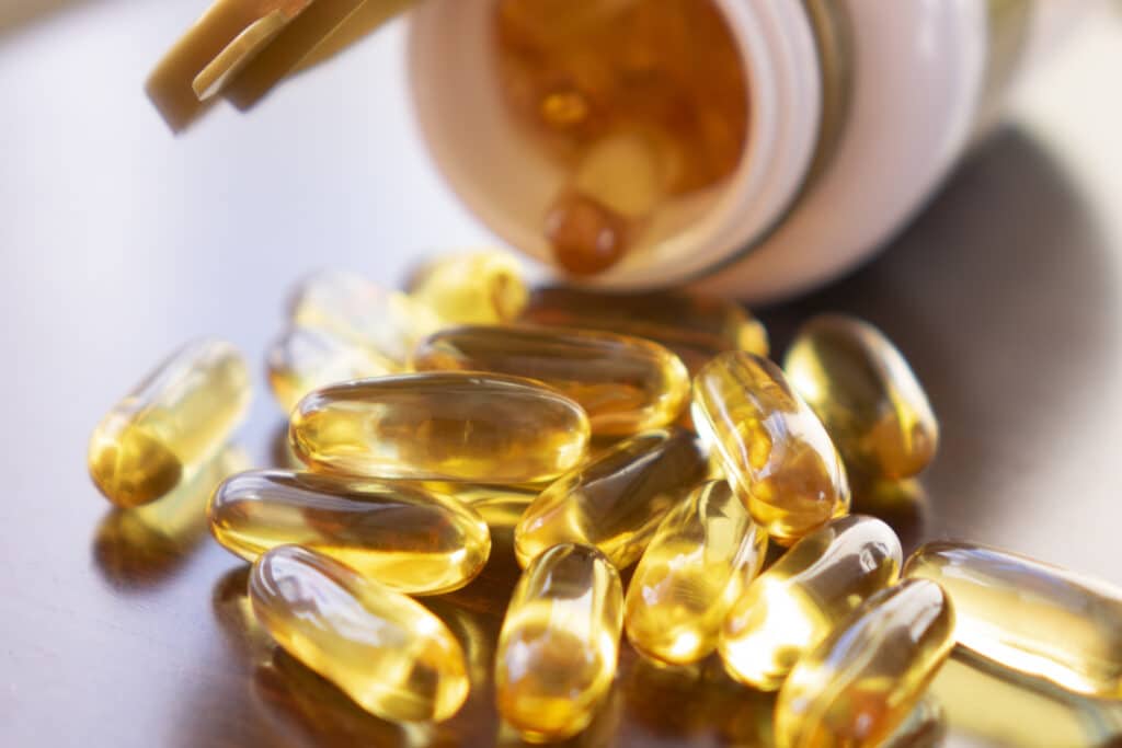 Fish Oil Capsules With Omega 3 And Vitamin D In A Glass Bottle On Wooden Texture, Healthy Diet Concept, Close Up Shot.