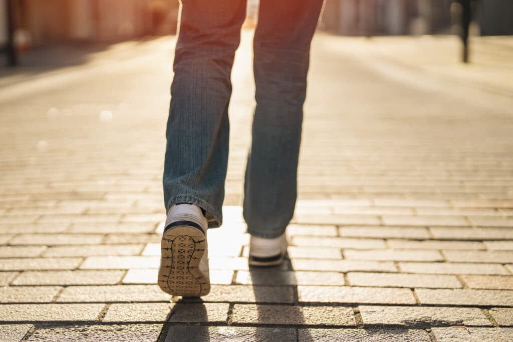 Legs Of Young Woman Student Having A Fun Time And Walking Along A Paved Street In The City At Sunset