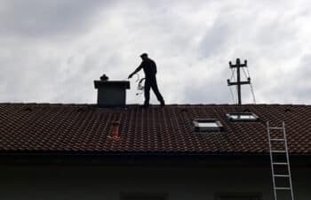 A Chimney Sweep Cleans The Chimney On A House Roof