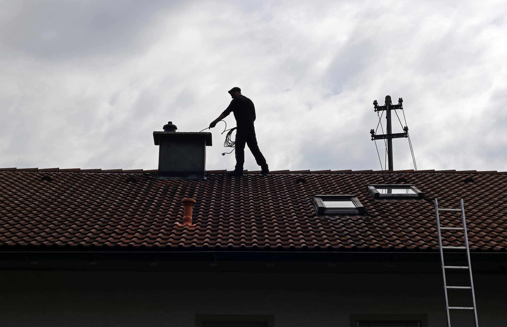 A Chimney Sweep Cleans The Chimney On A House Roof