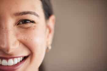 Face Of Beautiful Mixed Race Woman Smiling With White Teeth. Portrait Of A Woman's Face With Brown Eyes And Freckles Posing With Copy Space. Dental Health And Oral Hygiene