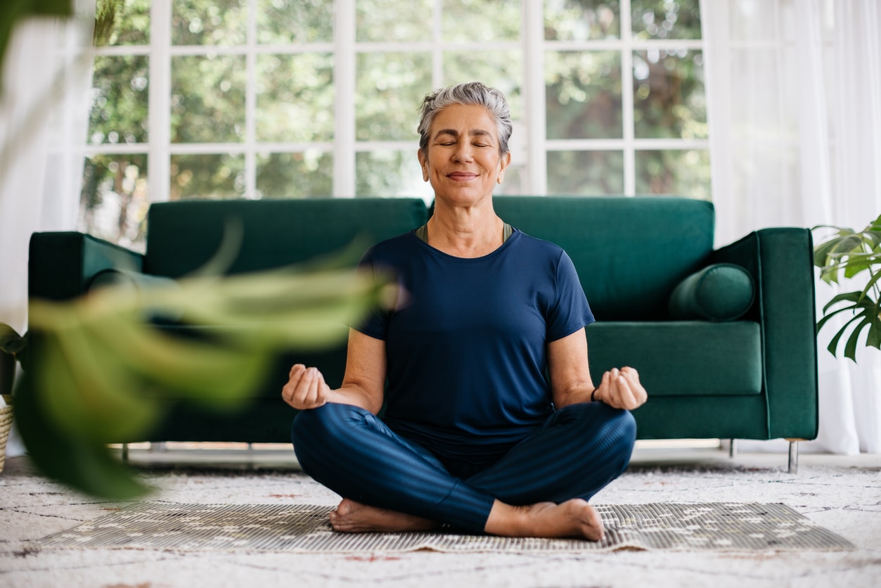 Relaxing The Mind And Finding Inner Peace With Yoga: Senior Woman Meditating At Home