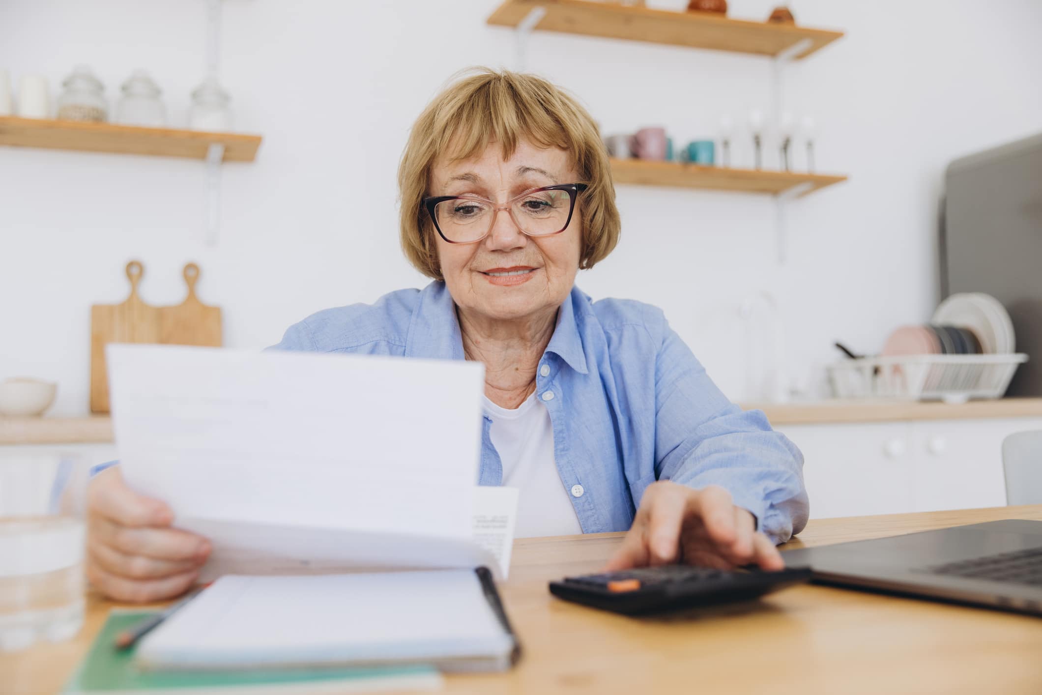 Senior Business Woman Holding Paper Bill Using Calculator, Old Lady Managing Account Finance, Calculating Money Budget Tax, Planning Banking Loan Debt Pension Payment Sit At Home Kitchen Table.