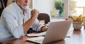 Cropped Shot Of Senior Man Using Laptop Checking Documents Indoor