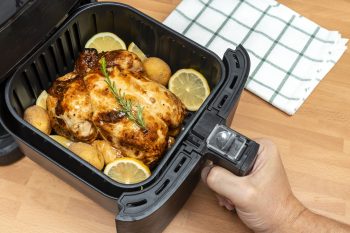 Hand Cooking Whole Roasted Chicken With Garnish In Air Fryer At The Kitchen. Top View.