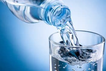 Pouring Water From Bottle Into Glass On Blue Background