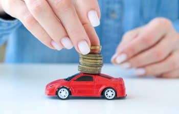 Female Hand Putting Coins In Stack On Red Toy Car. Saving Money To Buy A Car, Auto Loan, Automobile Insurance