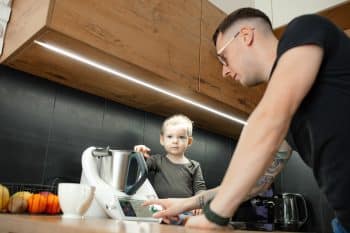 Mature Man In Glasses Search Recipe With Smart Thermo Mixer Display Program, Cook With Little Son In Kitchen. Father Day