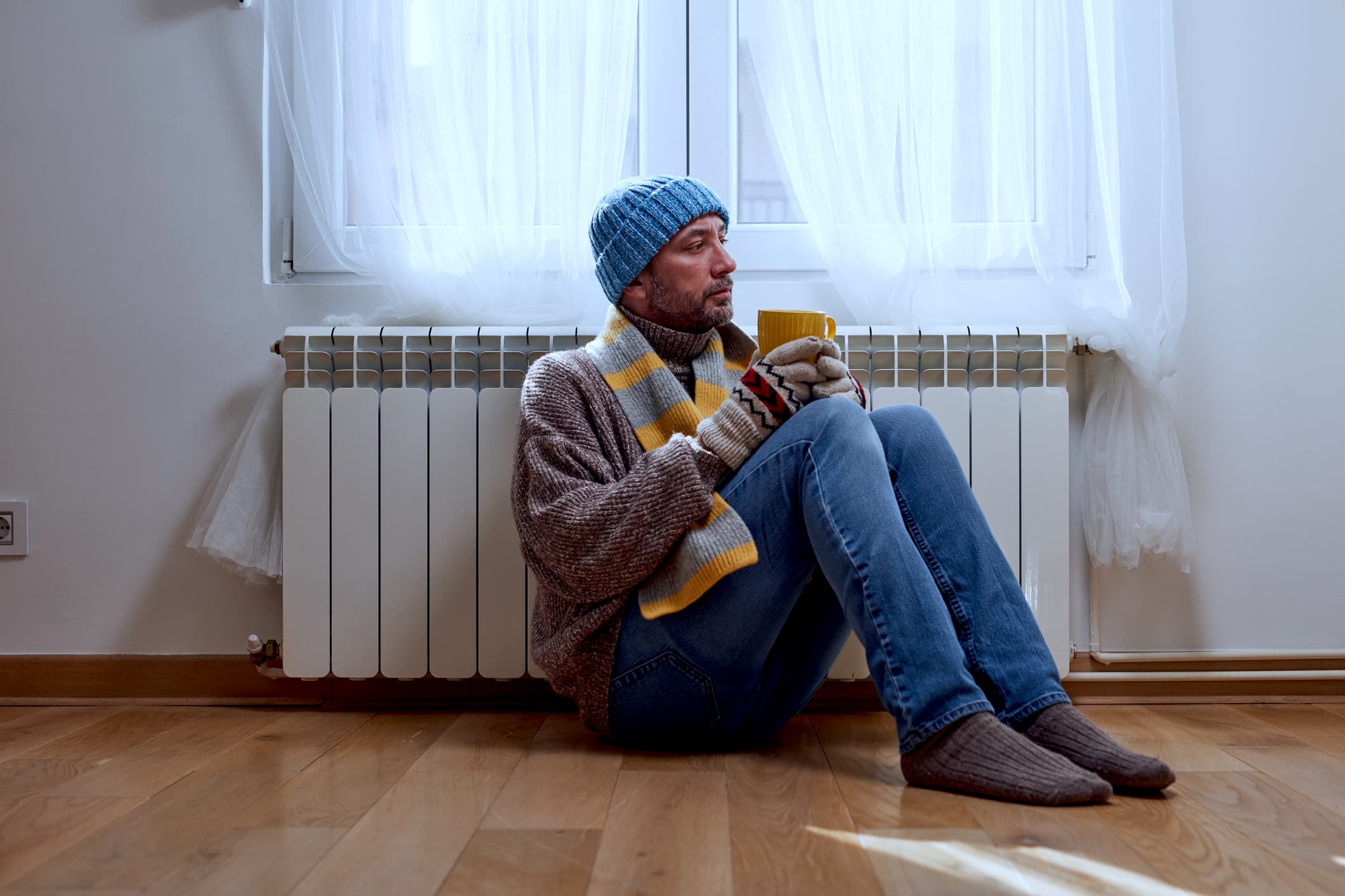 Man With Hat, Sweater And Hand Gloves Indoors On A Chilly Winter Day, Energy And Gas Crisis, Cold Room, Heating Problems.