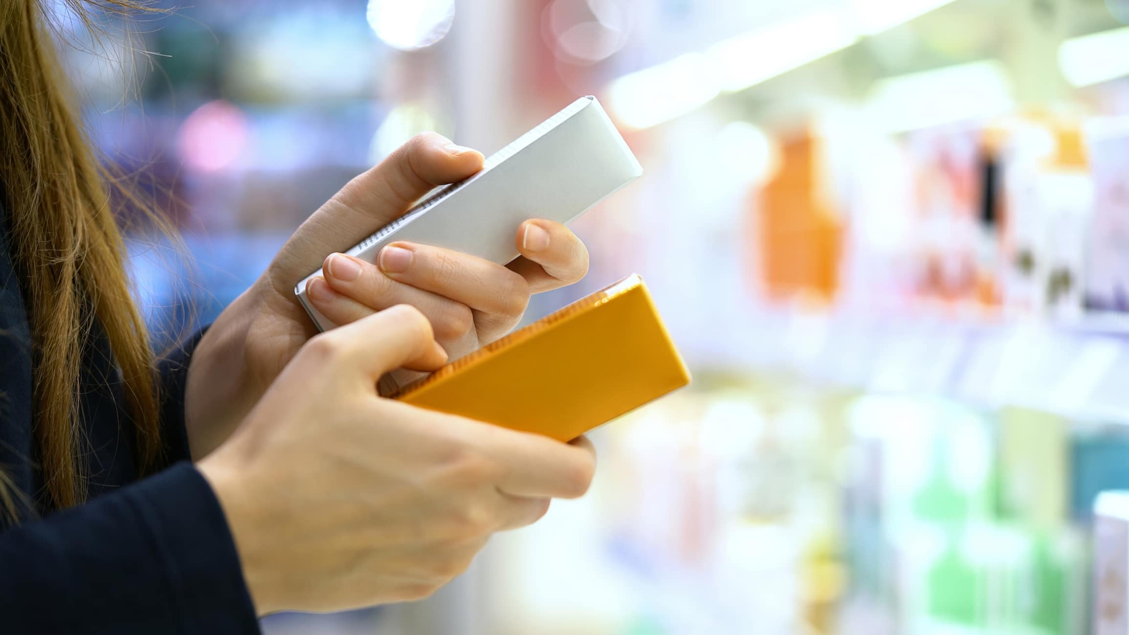 A Female Customer Compares Two Skincare Product, Reading Labels With Ingredients